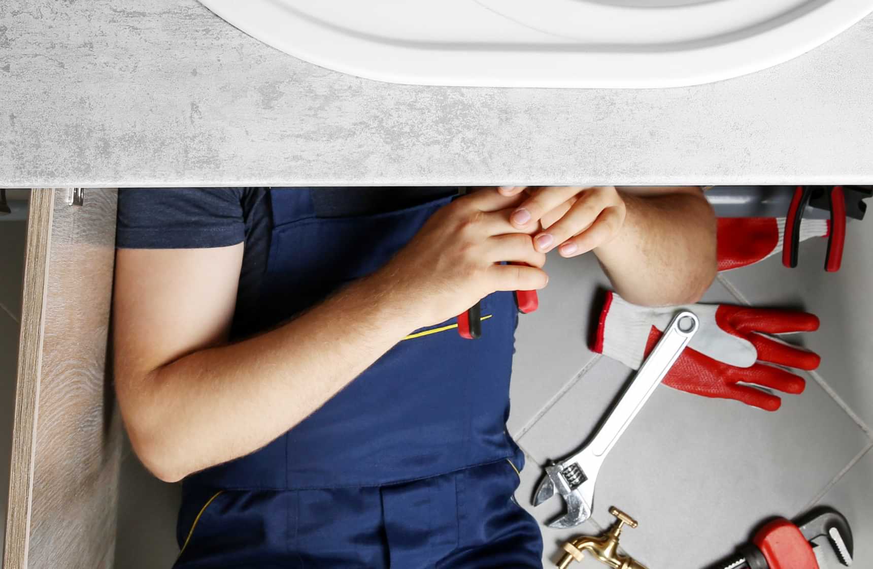 Plumber repairing pipes under a bathroom sink with tools nearby
