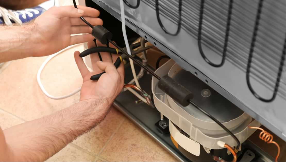 Technician repairing wiring and components behind a refrigerator