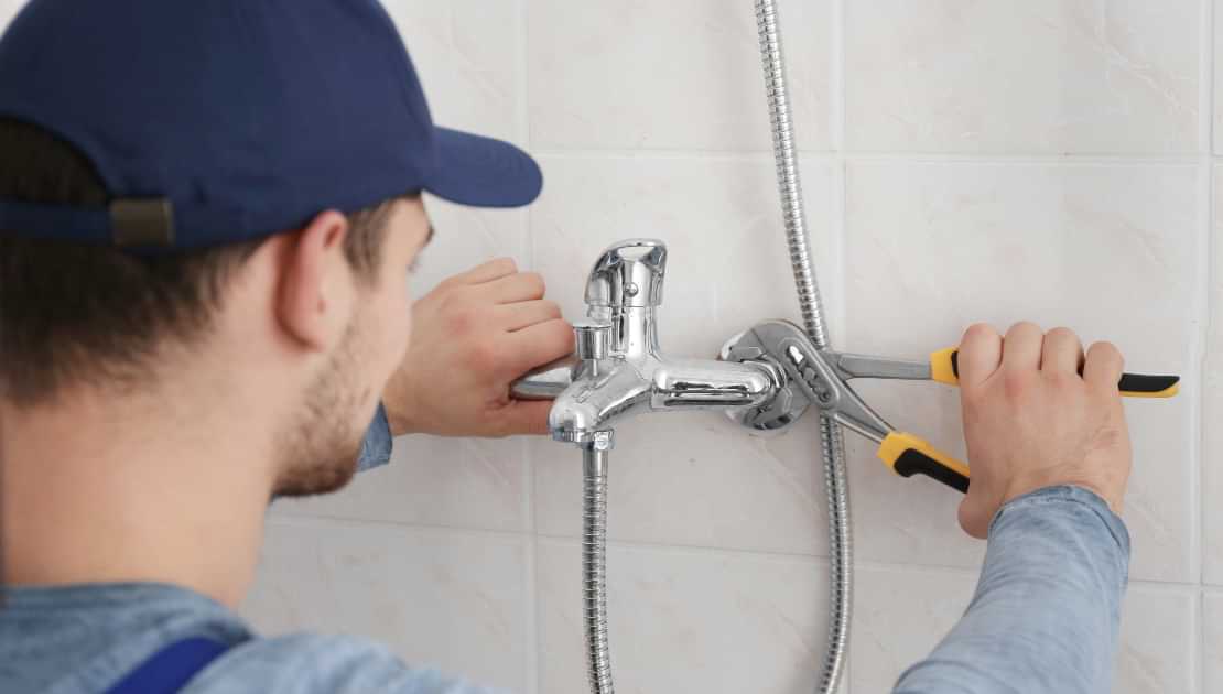 Technician repairing a shower faucet with pliers in a tiled bathroom