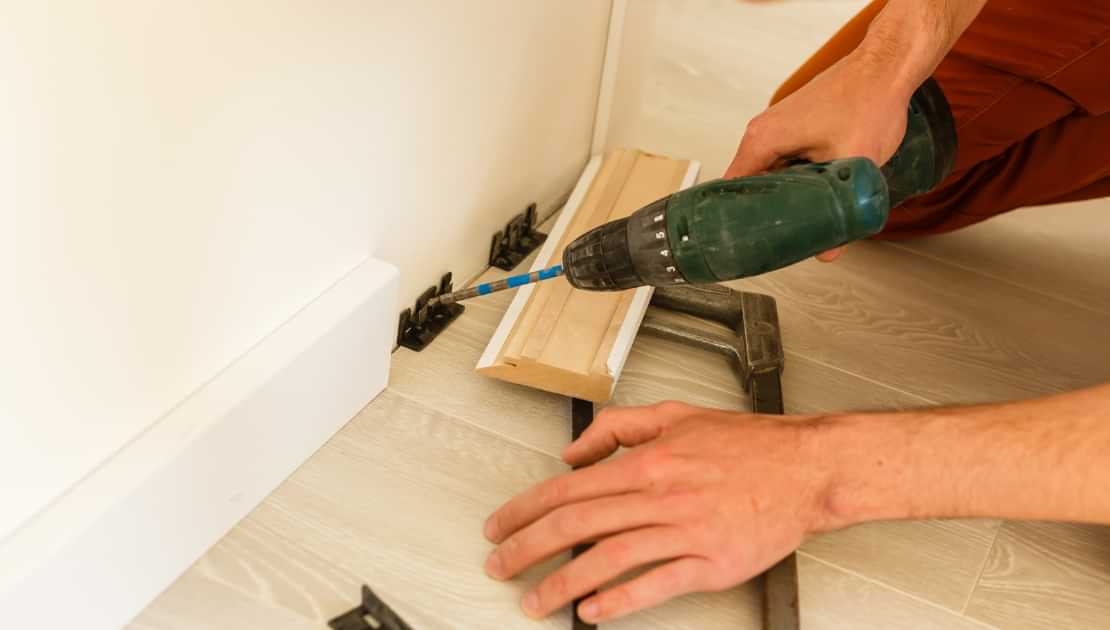 Handyman drilling skirting board brackets during home carpentry repairs