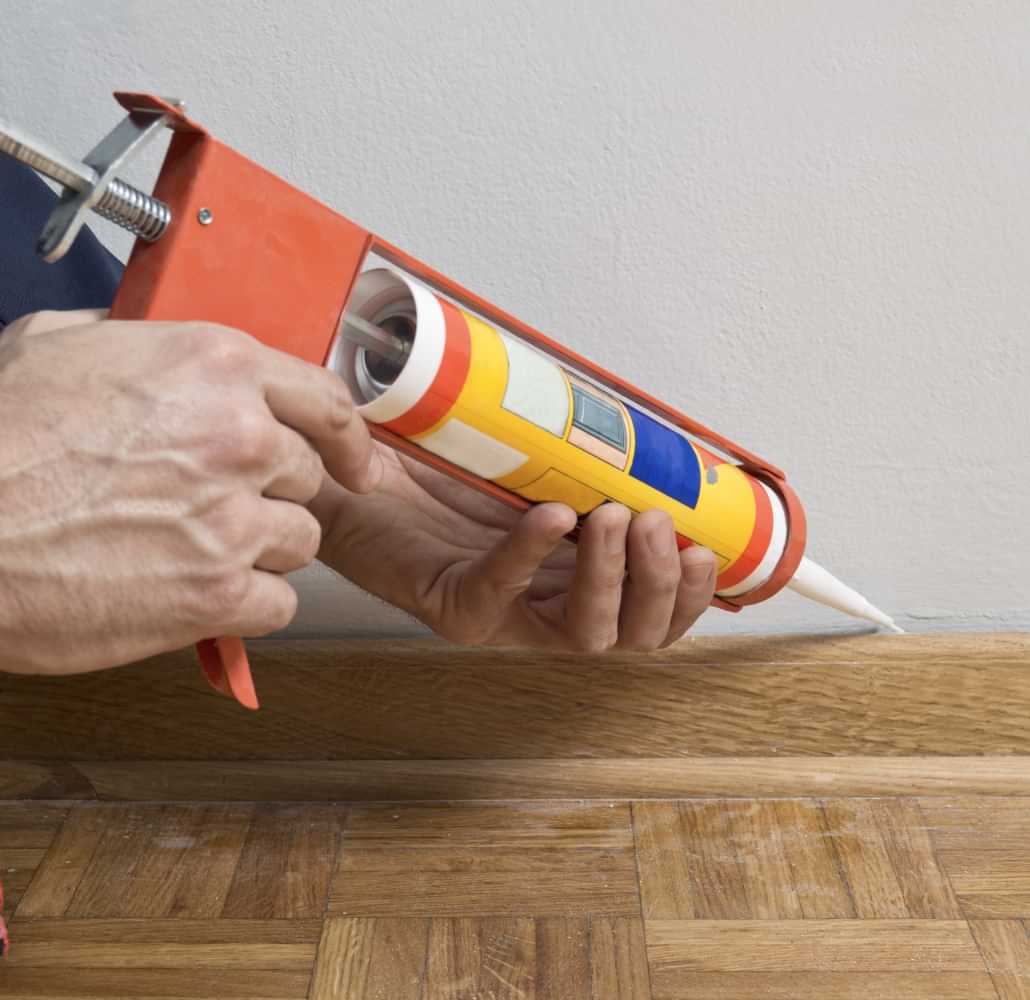 Technician applying caulk along a wall and floor joint