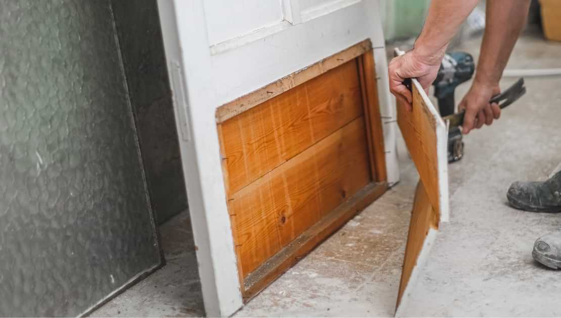 Handyman removing a damaged wooden door panel during door repair