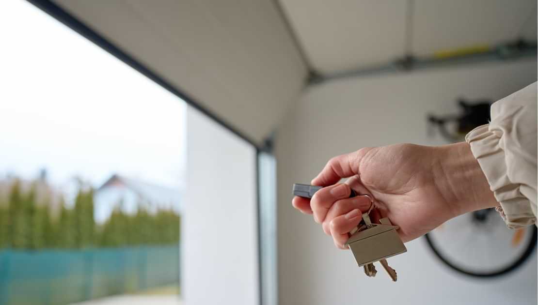 Hand holding keys and remote inside an open garage door