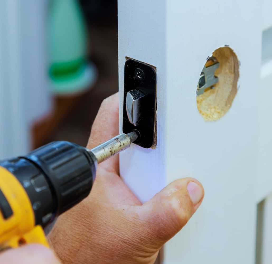 Technician installing a door latch with a drill