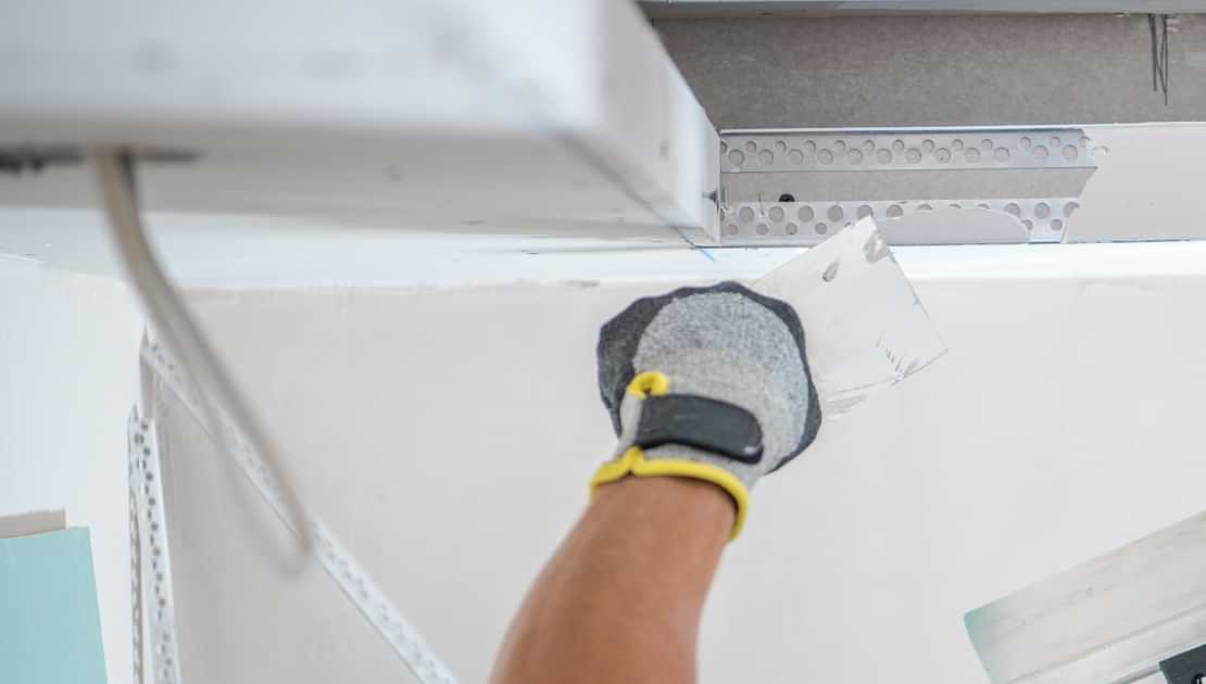 Worker applying joint compound to a ceiling during drywall repair