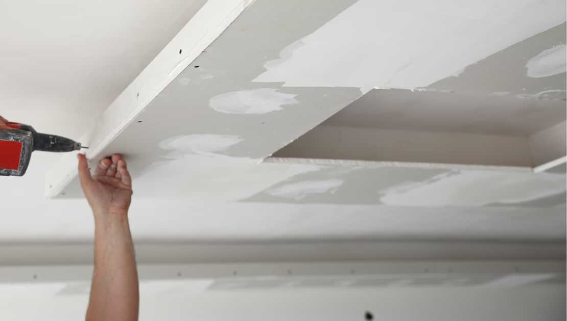 Handyman fastening drywall to the ceiling during interior repair work