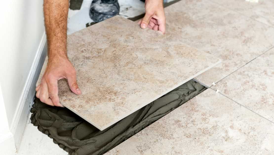 Large floor tile being laid into adhesive during tiling installation