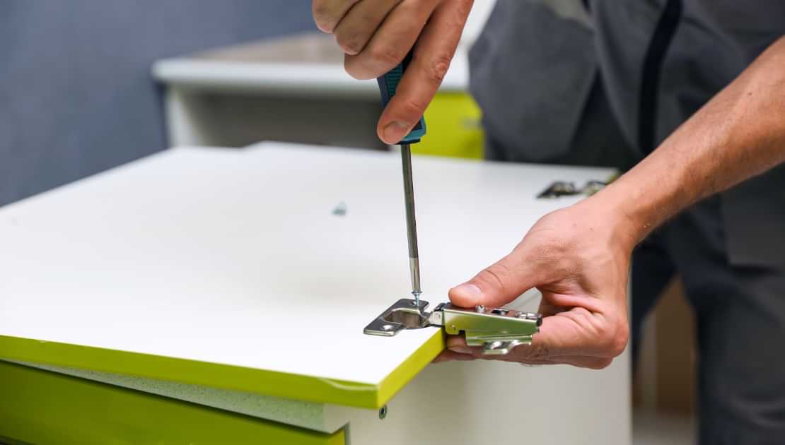 Attaching a cabinet hinge with a screwdriver during furniture assembly