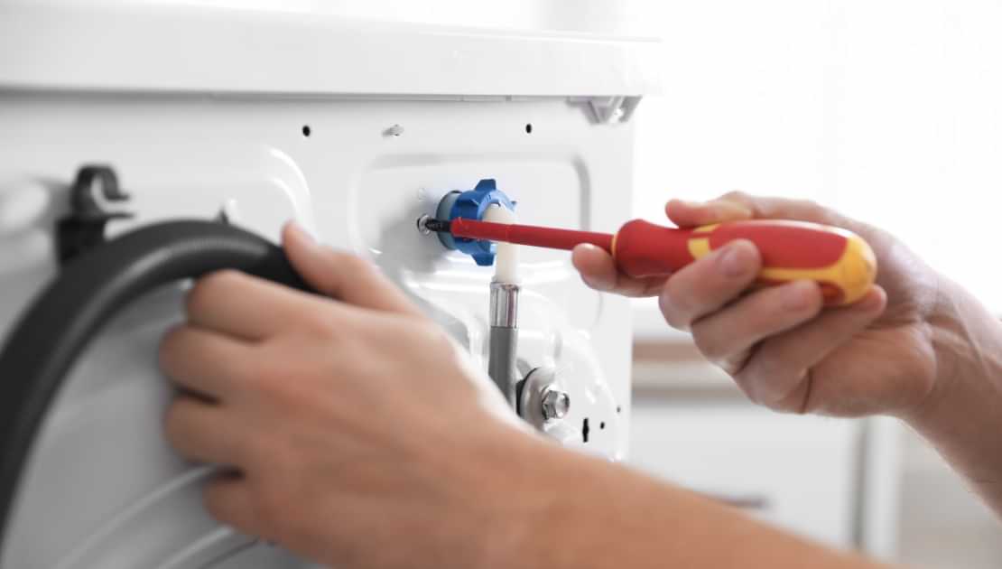 Tightening a washing machine water connection with a screwdriver during appliance repair