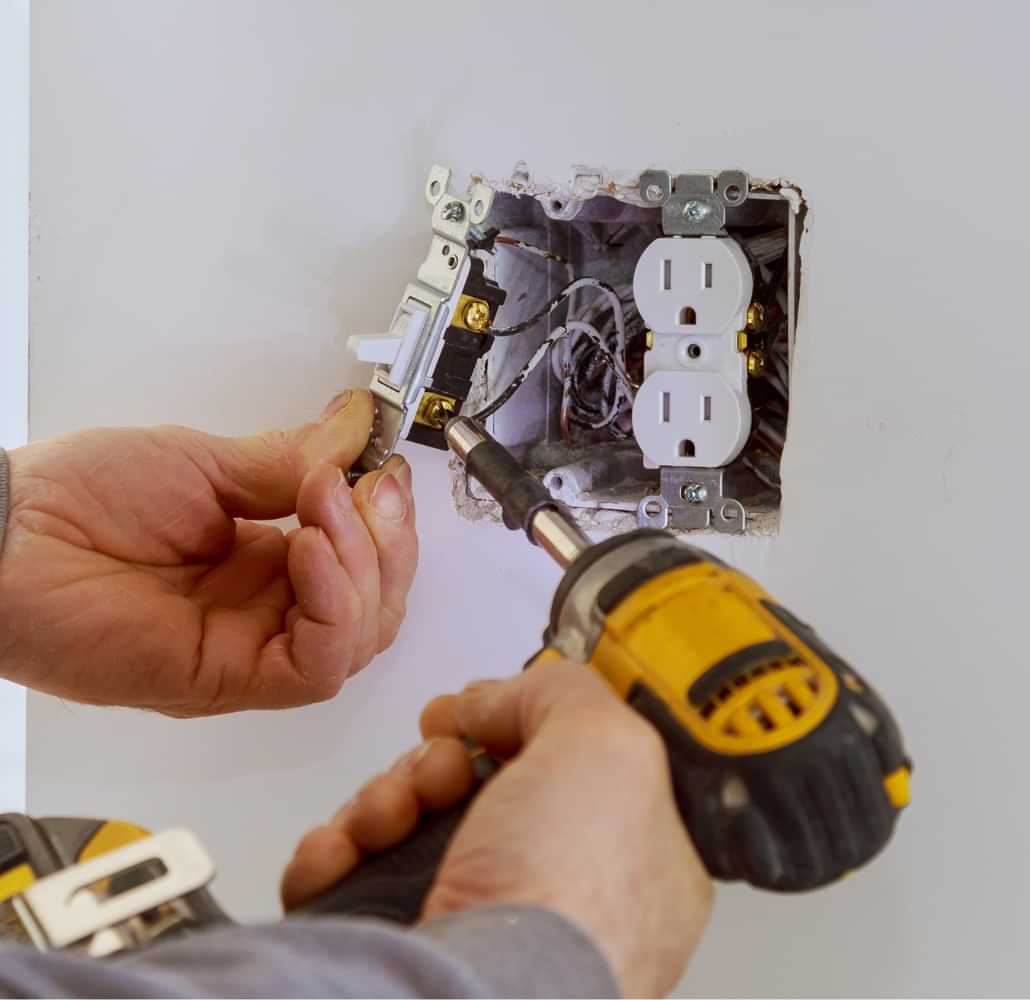 Technician repairing an electrical outlet with a drill