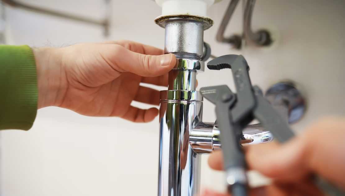 Tightening sink drain pipe connection with pliers during plumbing repair