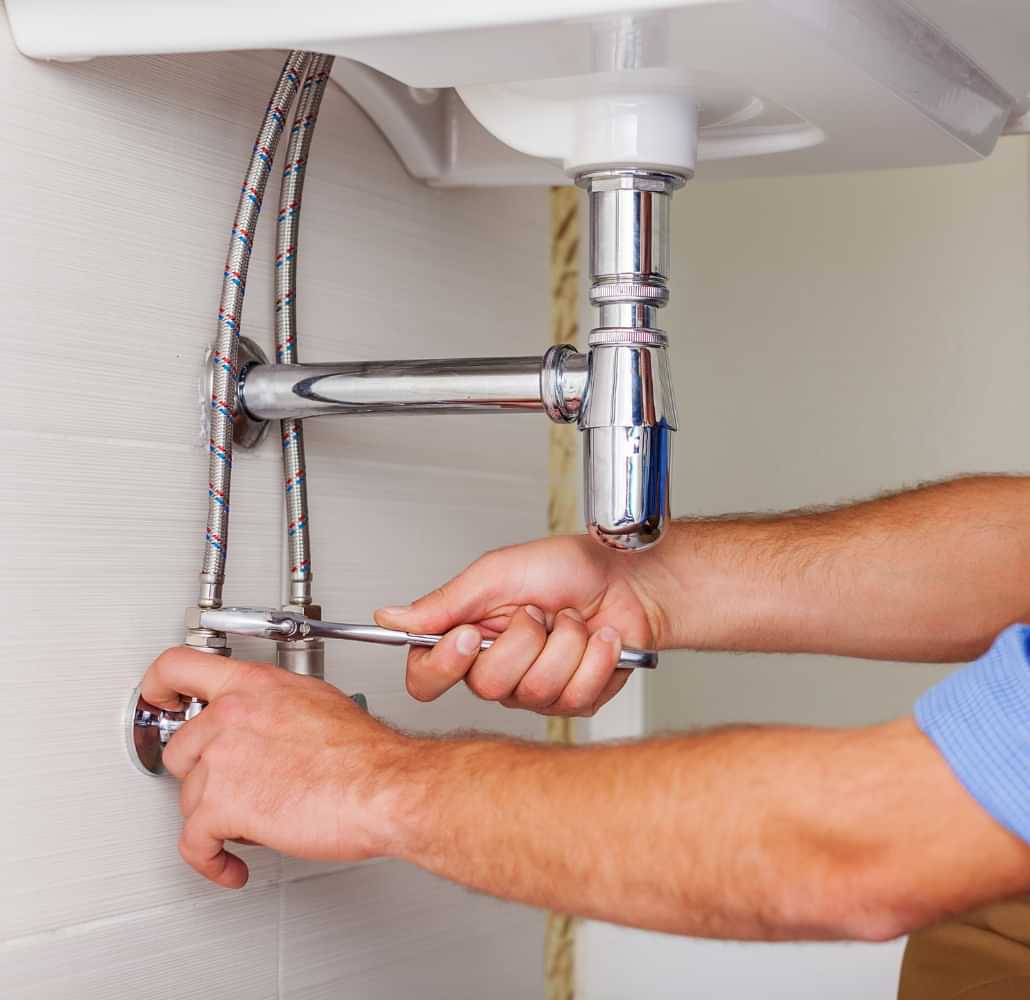 Technician repairing sink plumbing under a basin