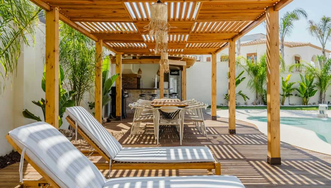 Wooden pergola and deck seating area by a backyard swimming pool