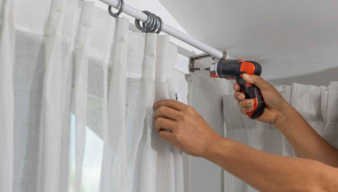 Fitting a curtain rod bracket with a cordless drill during curtain installation