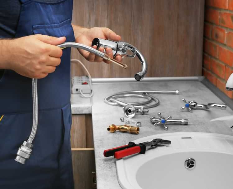 Plumber repairing a bathroom sink faucet with tools on the countertop